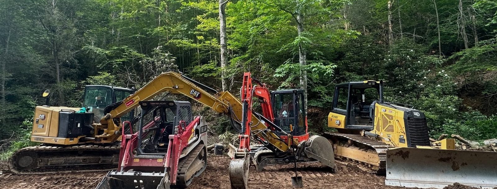 Excavators, a track loader and a dozer staged on a wooded job site